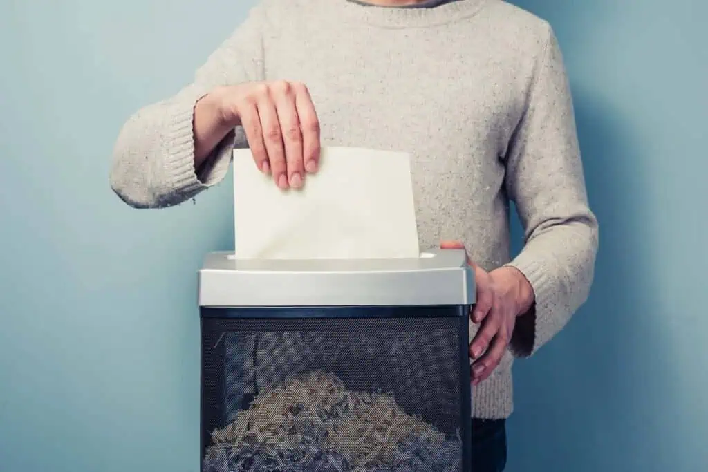 a man in a gray sweater shreds a document into a paper shredder