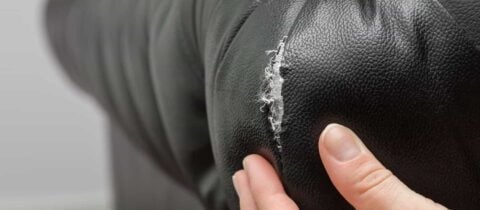 an image of a torn black couch with someone&#039;s hand prodding at the damage