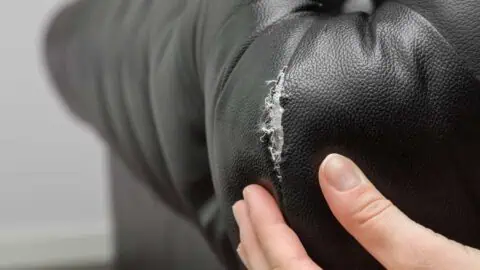 an image of a torn black couch with someone's hand prodding at the damage