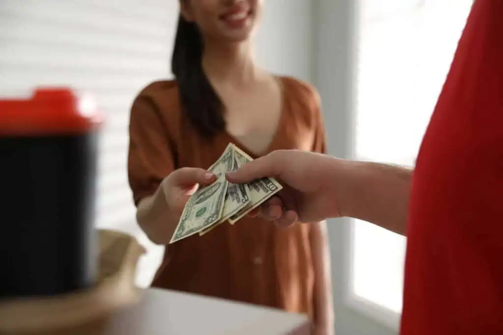 a woman hands over a tip to a delivery driver in a red shirt
