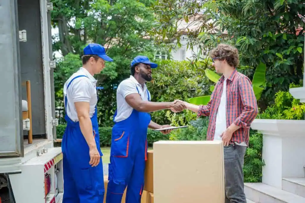 a man shakes the hand of two movers in blue overalls