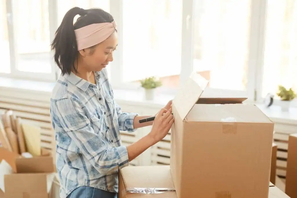 A woman writes a label in black marker on the side of a moving box
