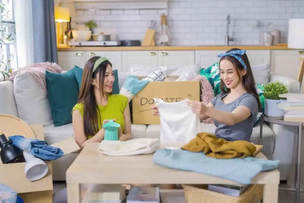 Two women look through clothing and other items to organize them into donation boxes