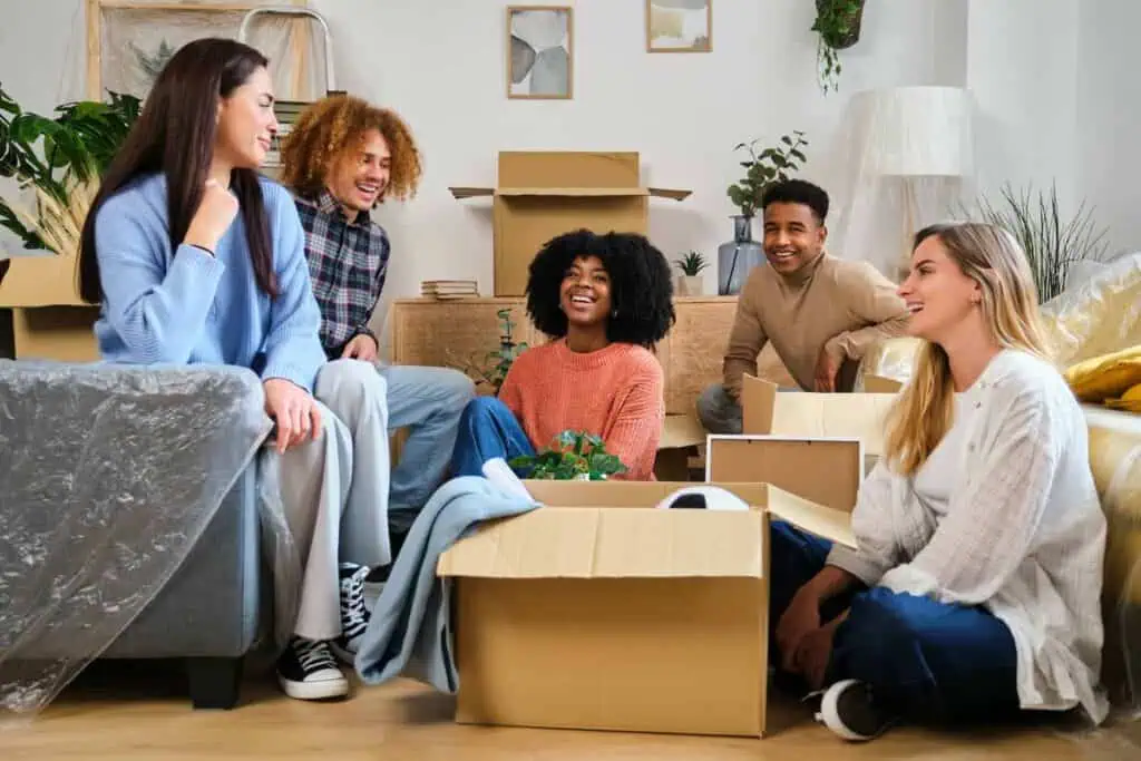 a group of young adults chats and laughs in a room full of moving boxes