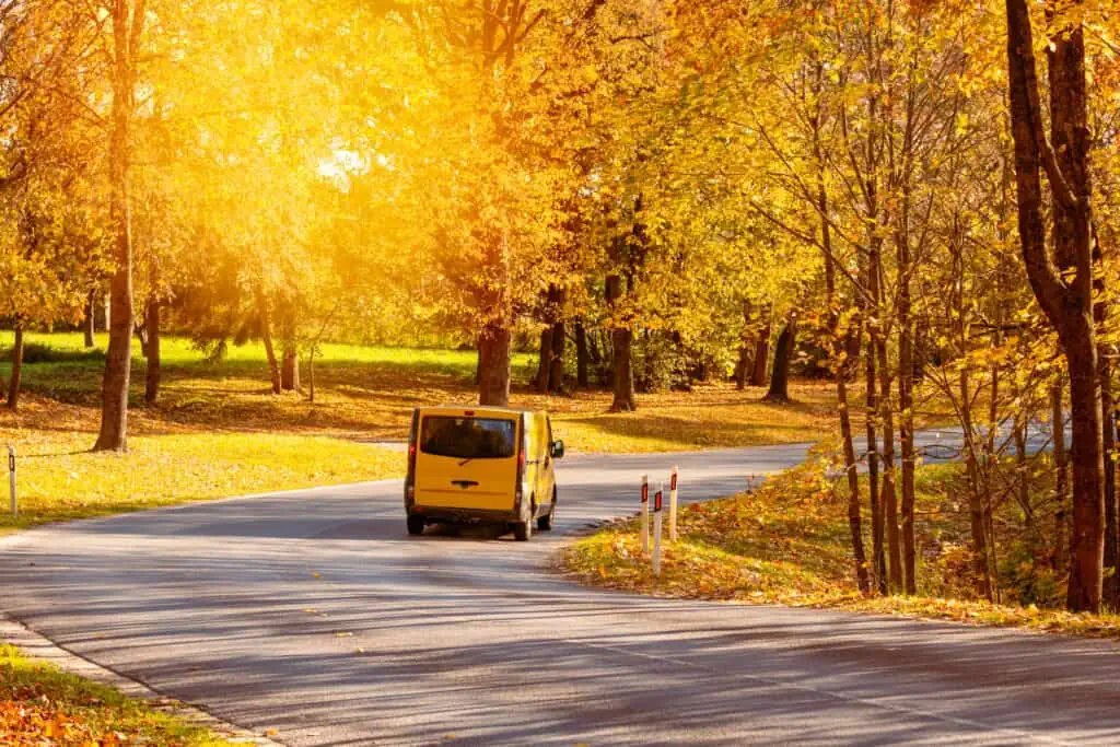 a yellow moving truck drives down a road lined with trees in autumn colors