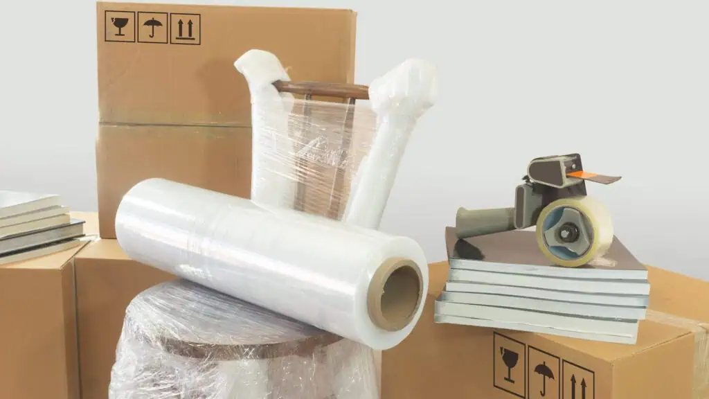 stacked boxes are in the background behind a chair wrapped in shrink wrap and tape