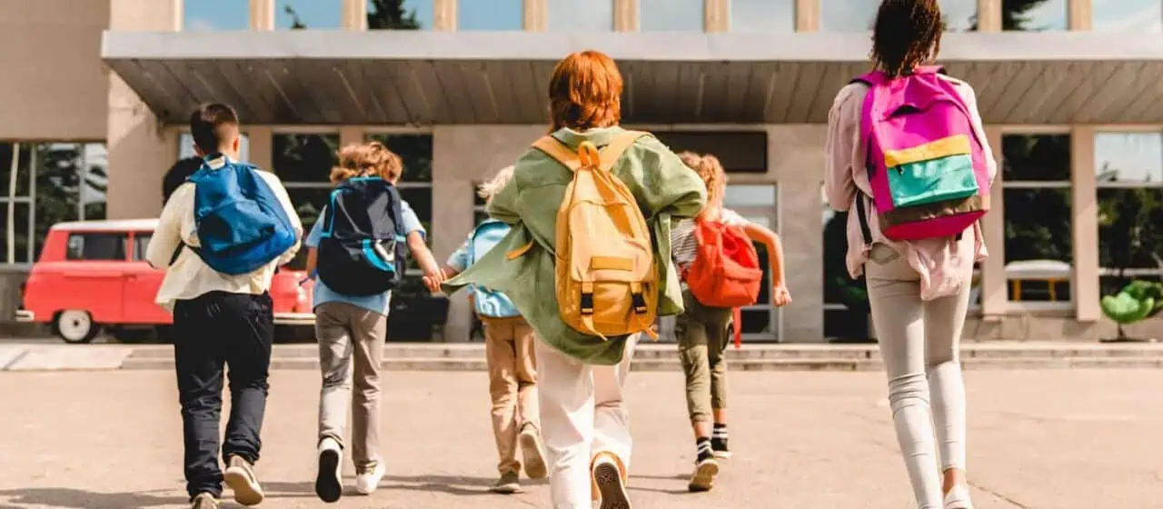 a group of children all wearing colorful backpacks run happily towards their school building