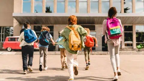 a group of children all wearing colorful backpacks run happily towards their school building