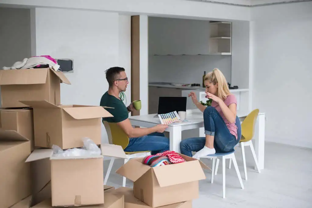two people planning and talking about their move at a kitchen table. there are several packed boxes stacked to the left side of the shot.