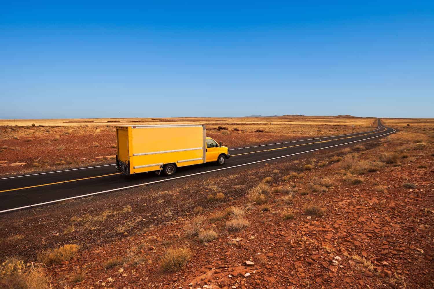 a yellow moving truck driving through the desert