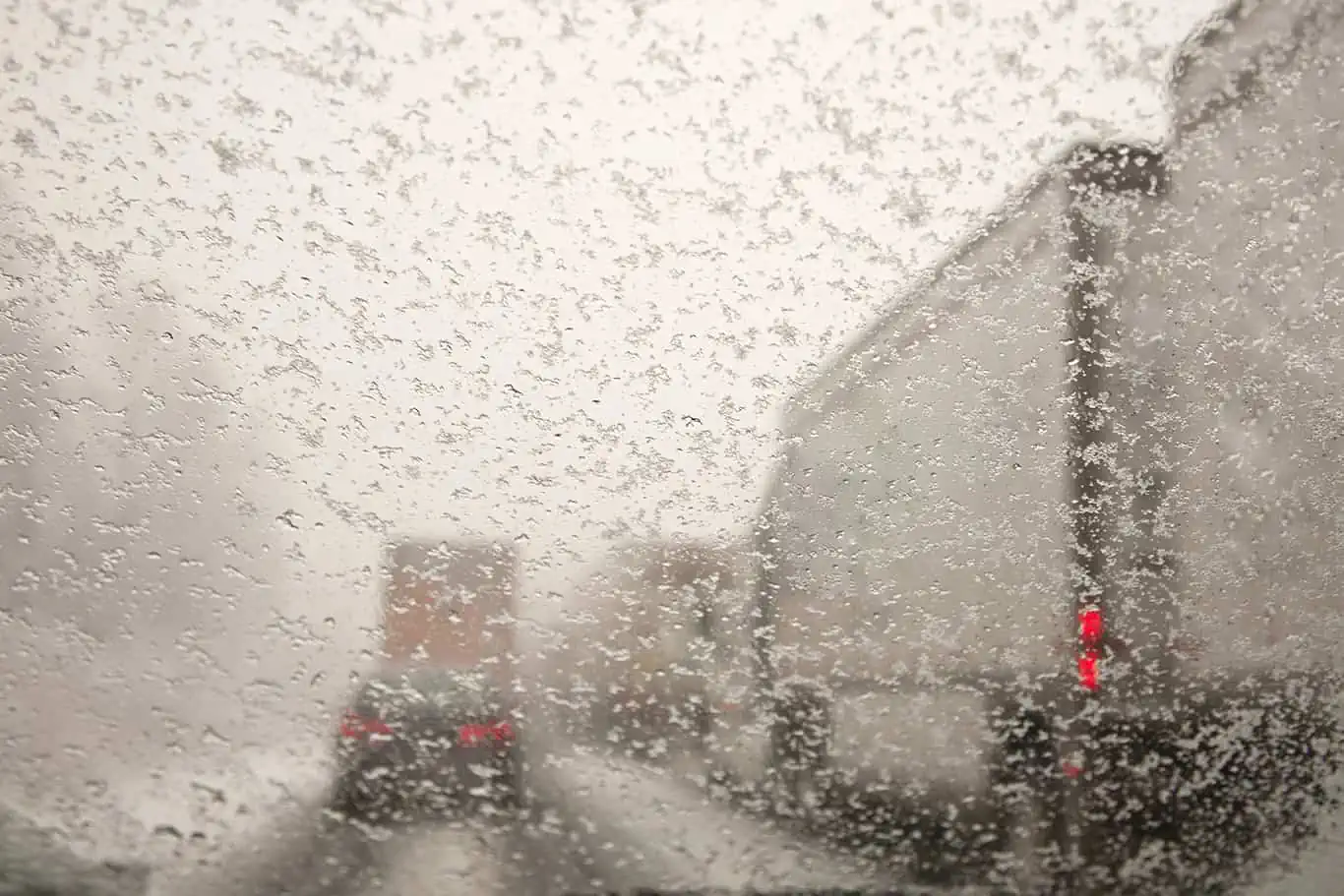 Cars and trucks driving on snow packed roads taken through a windshield covered with snowflakes.