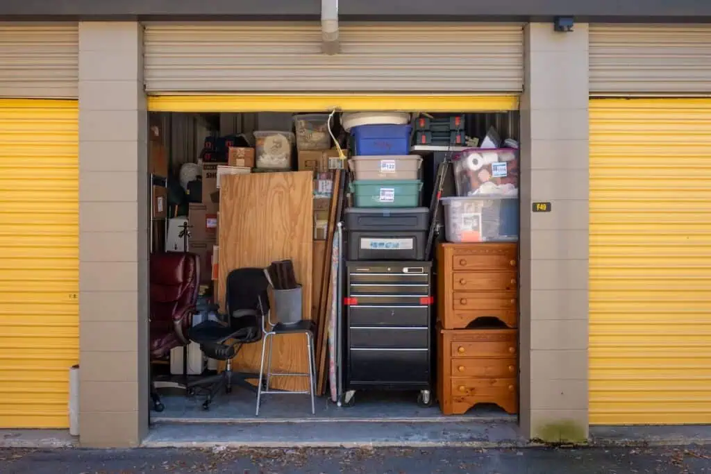 An open storage unit showing its contents, which include folding chairs, a tool chest, side tables, and storage bins