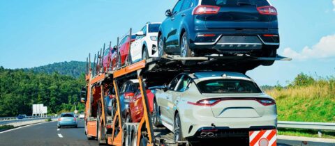 Two decks of cars being towed along a highway