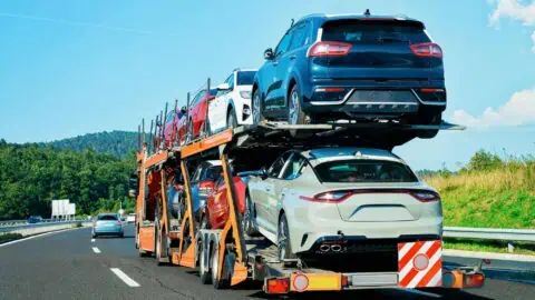 Two decks of cars being towed along a highway