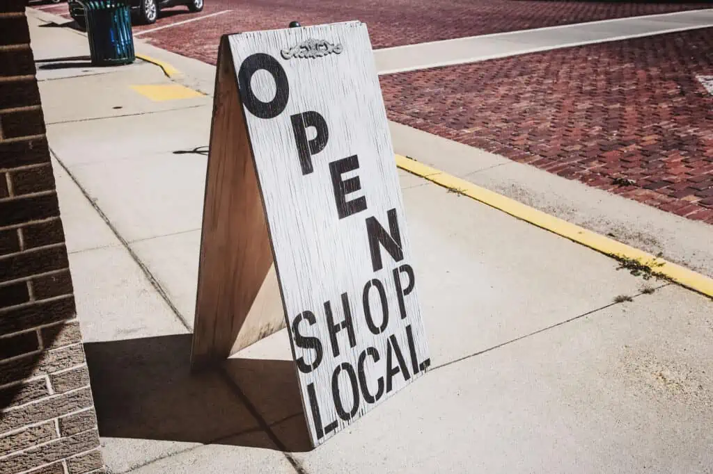 white wooden signboard that reads "open, shop local" in black letters. Using local SEO to improve your digital presence can attract customers in your area the same way a physical sign can.