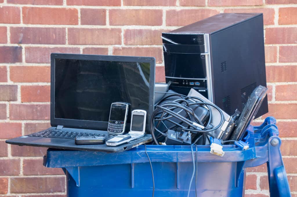 a trash can filled with electronic waste, a laptop and several cell phones are set at the very top