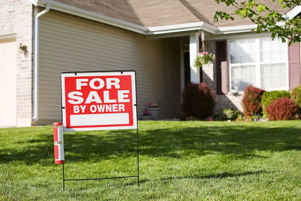 a real estate "for sale" sign outside of a home with white walls and a tan roof 