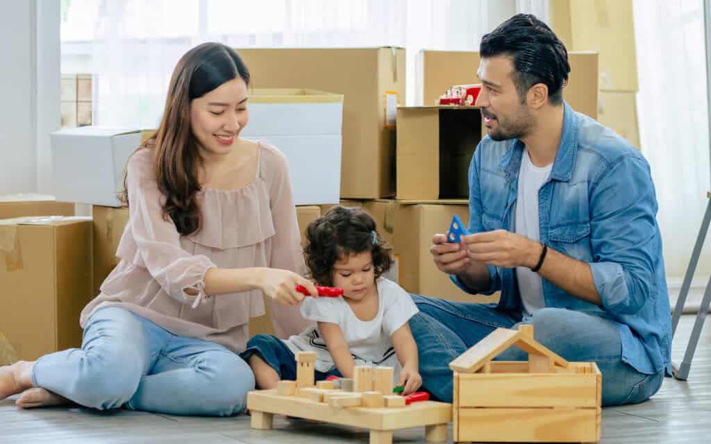 A family with a toddler plays with blocks in front of stacked moving boxes