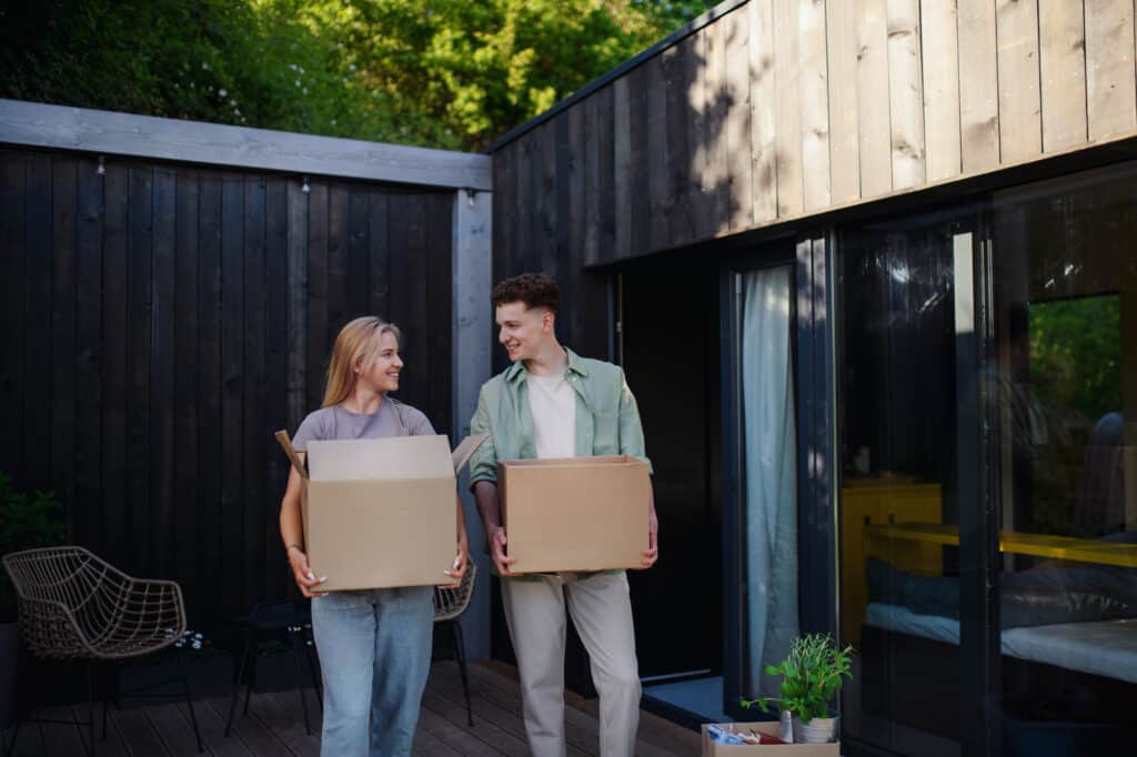 a man and a woman carrying cardboard boxes move into a tiny home