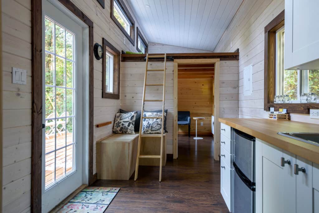 the interior of a tiny home with a ladder that leads up to a loft bed and multiple windows