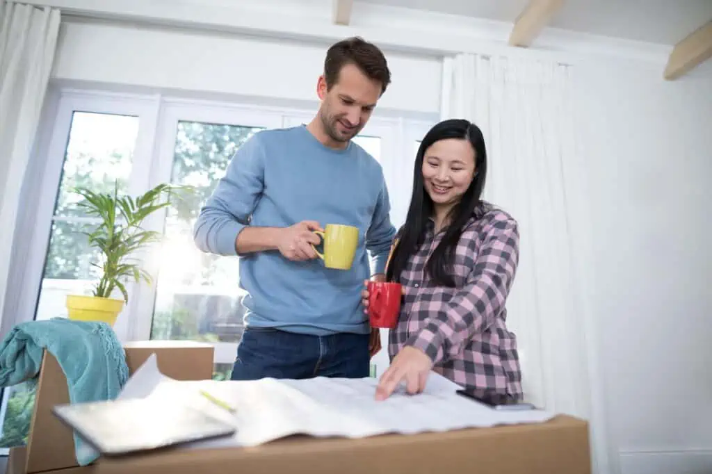 a pregnant couple looks over the blueprint of a home while holding mugs