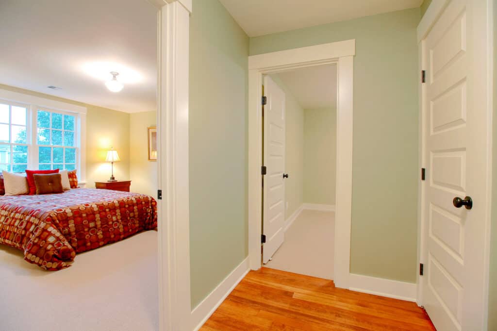 a hallway painted mint green opens up into two bedrooms set next to each other. One has a view of a queen sized bed with a dark red bedspread. 