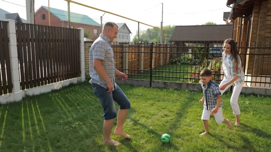 a family plays soccer in a fenced in yard