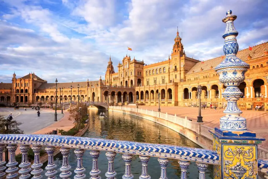 Plaza de Espana in Seville, Spain, at sunset. The view is over a bridge's railing and towards the canal that runs through the square in a circle