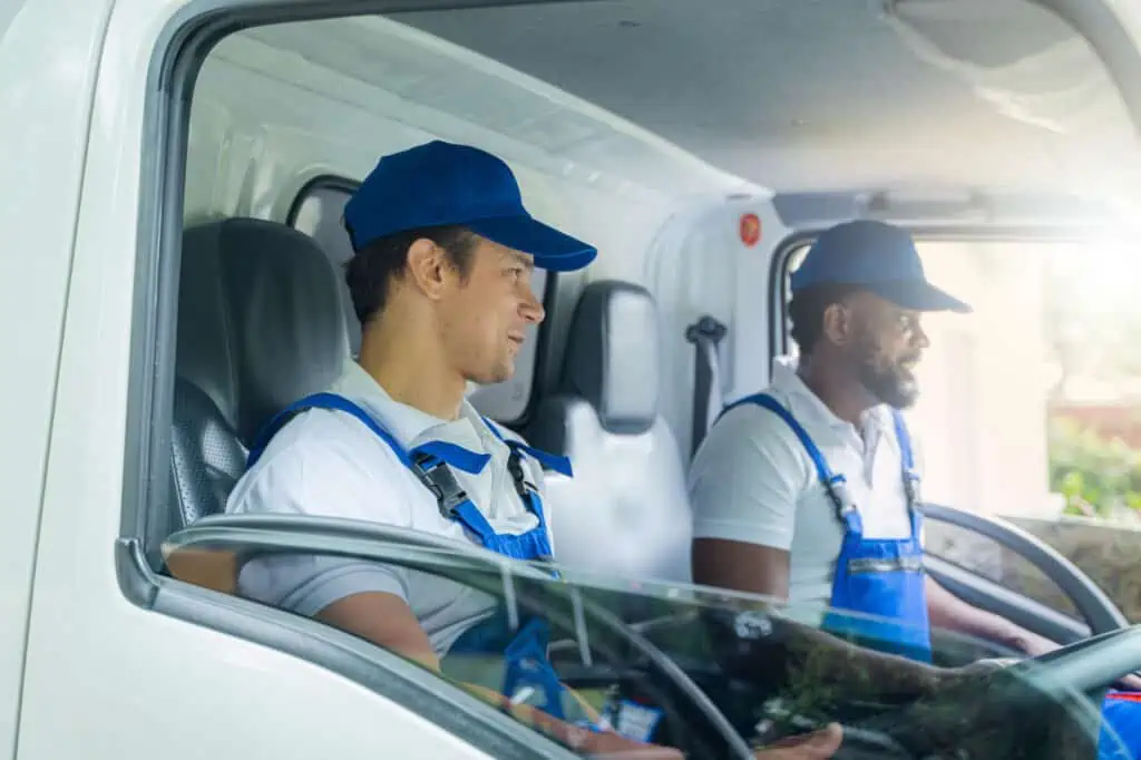 two workers in blue overalls sit in the cab of a moving truck