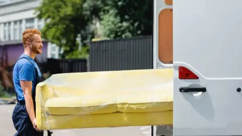 a moving company worker loads a yellow couch into a truck