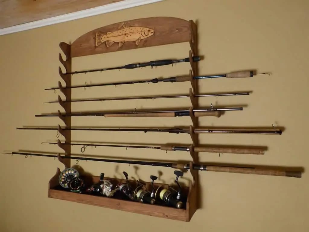 a wooden wall rack that holds fishing rods horizontally. The reels of the rods are set in a shelf at the bottom of the rack.