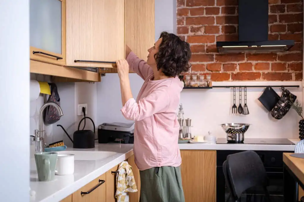a woman reaches into the back of an open kitchen cabinet