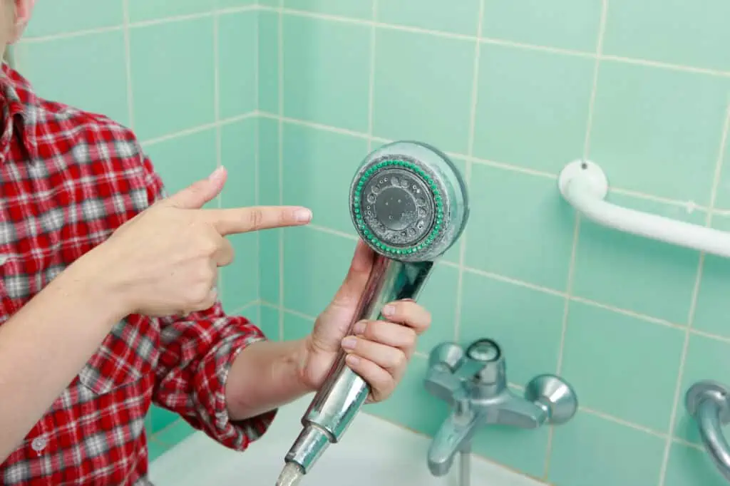 a person out of frame holds and points at a shower head with hard water stains on it 