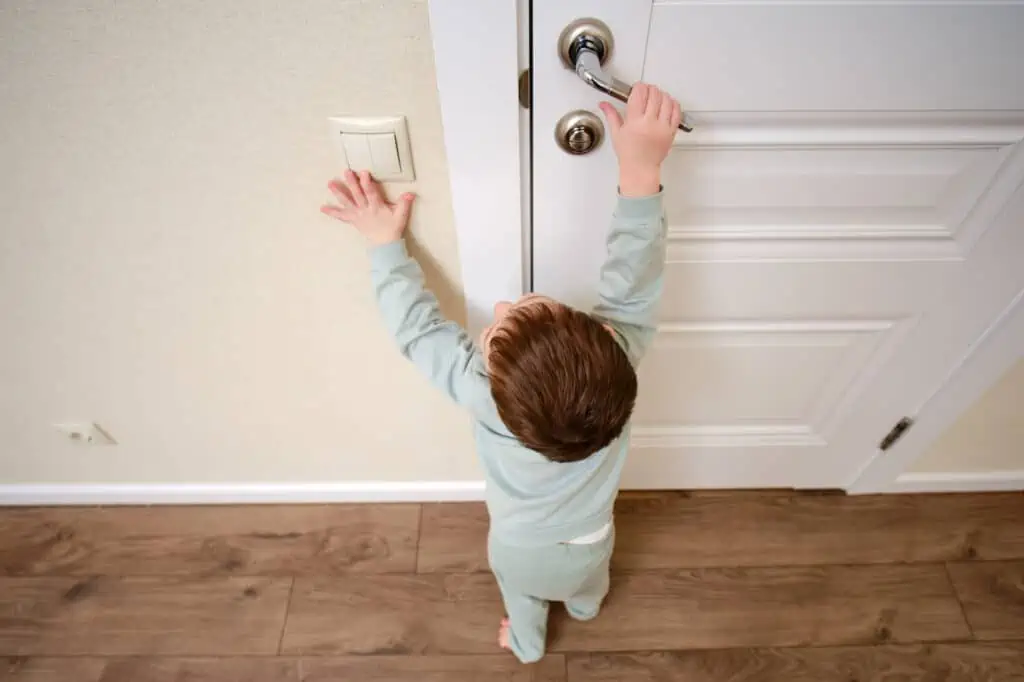a toddler turns a light off and opens a door as they exit a room