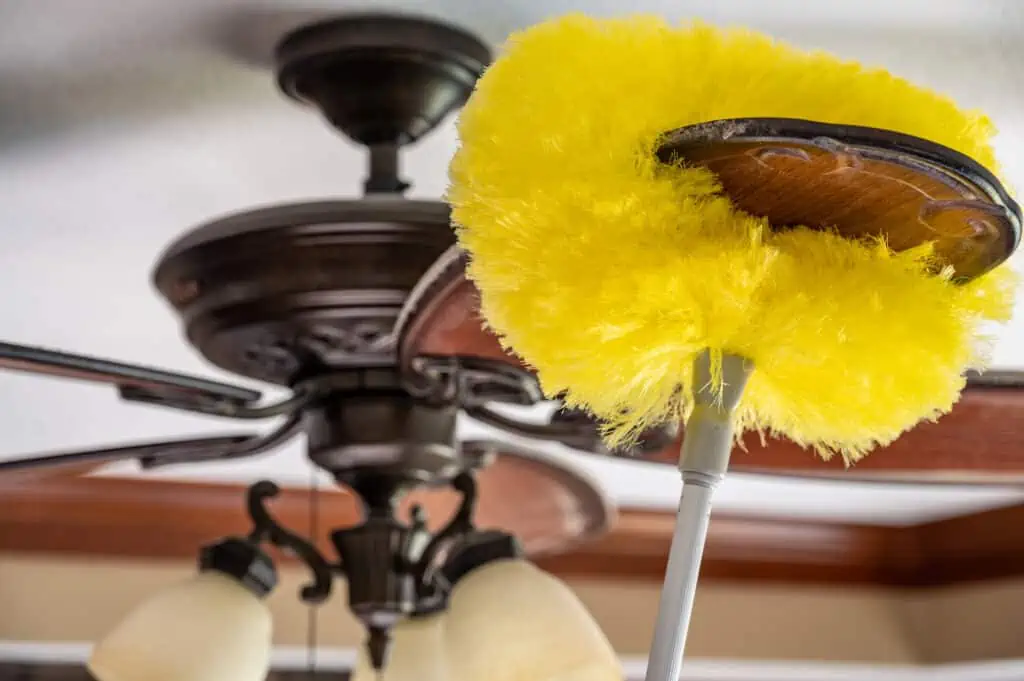a yellow dust cleaner is wiped along the top of the blades of a ceiling fan