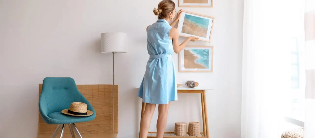 a woman wearing a blue dress hangs up paintings to decorate a small apartment