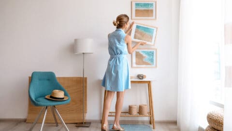 a woman wearing a blue dress hangs up paintings to decorate a small apartment