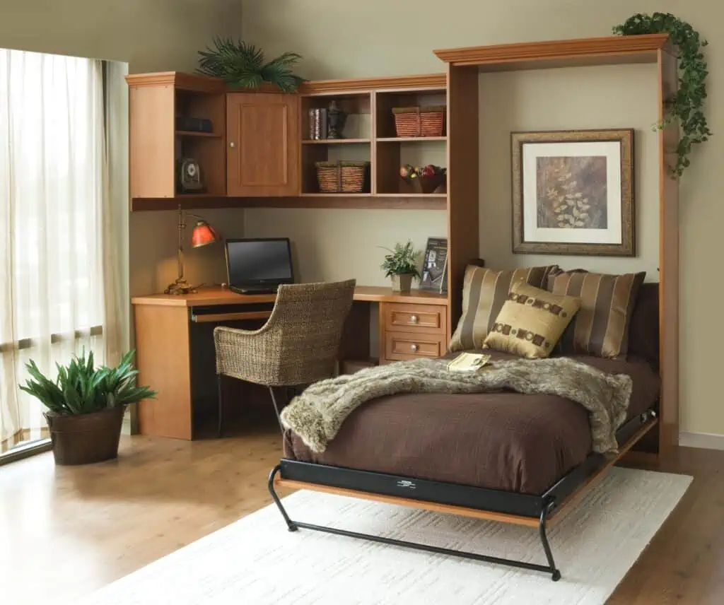 a murphy bed with brown sheets and patterned pillows is built into a corner desk set up. There is plenty of storage space for a small apartment