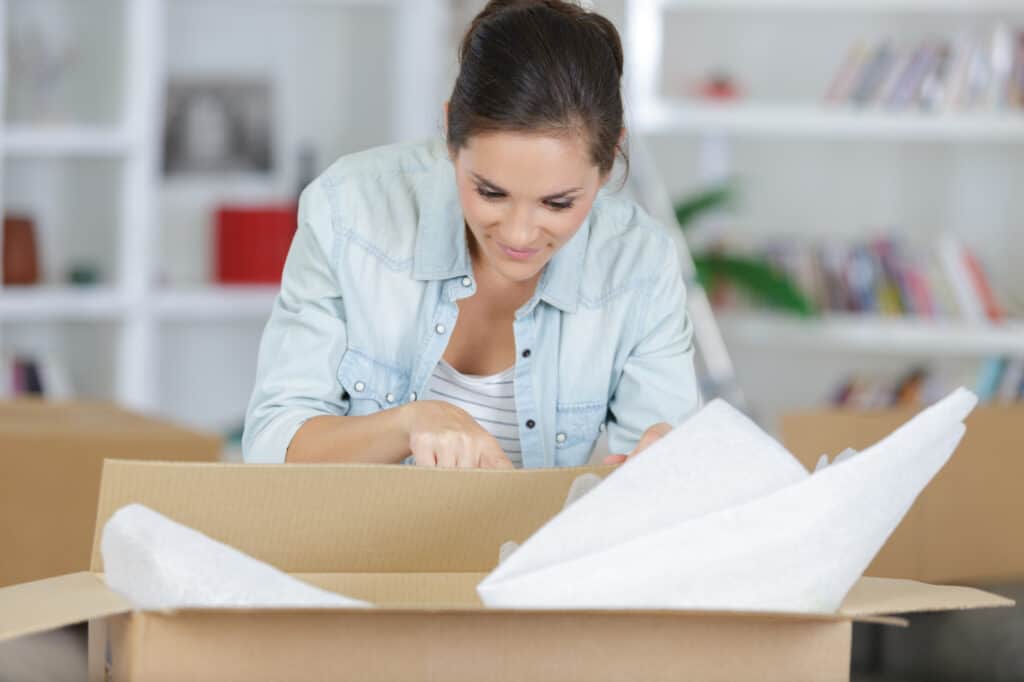 a woman checks a cardboard box in preparation for packing. There is packing paper inside. 