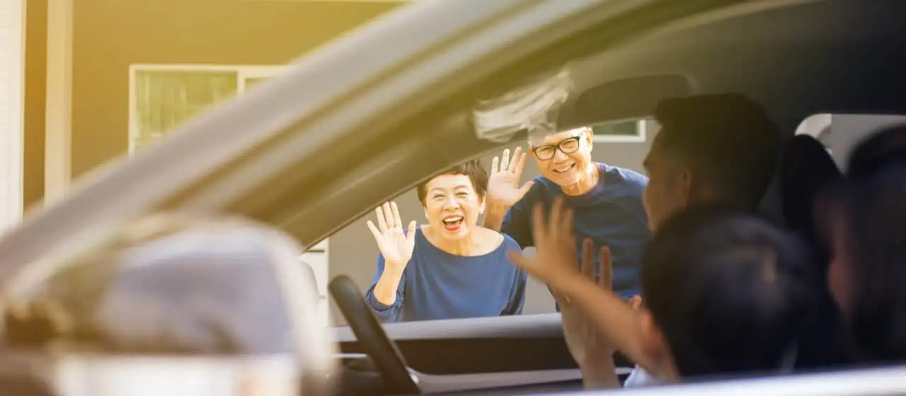 elderly parents wave to their adult child and grandchild in a car