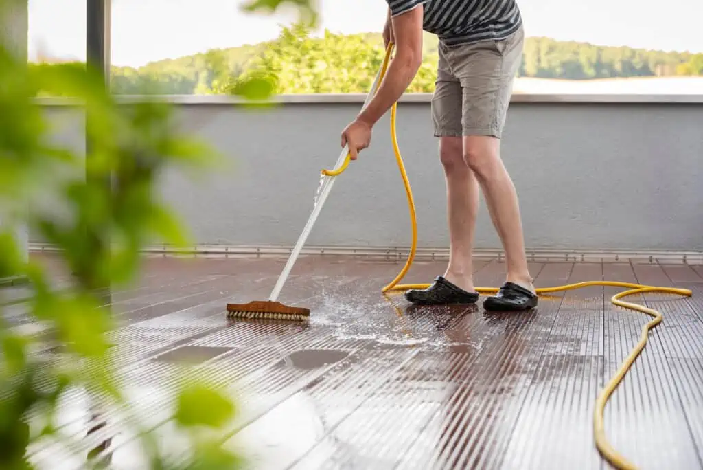 a person cleans off their deck with water and a brush