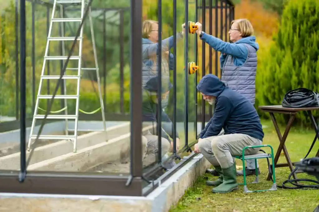 an older man and woman work on removing the glass from the side of a greenhouse