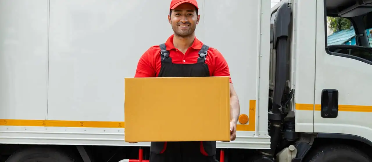 a mover that's part of a moving crew stands smiling in front of a moving truck