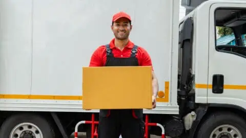 a mover that's part of a moving crew stands smiling in front of a moving truck