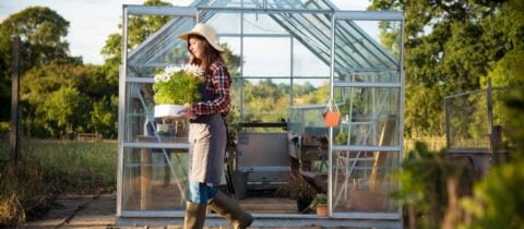 a woman walking out of a greenhouse carrying a bunch of flowers