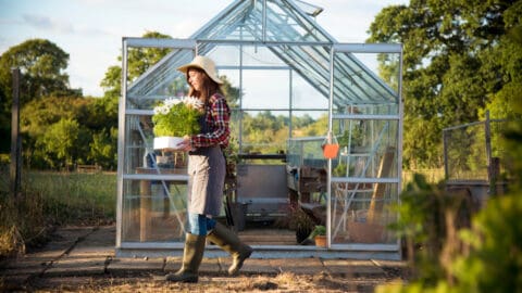 a woman walking out of a greenhouse carrying a bunch of flowers