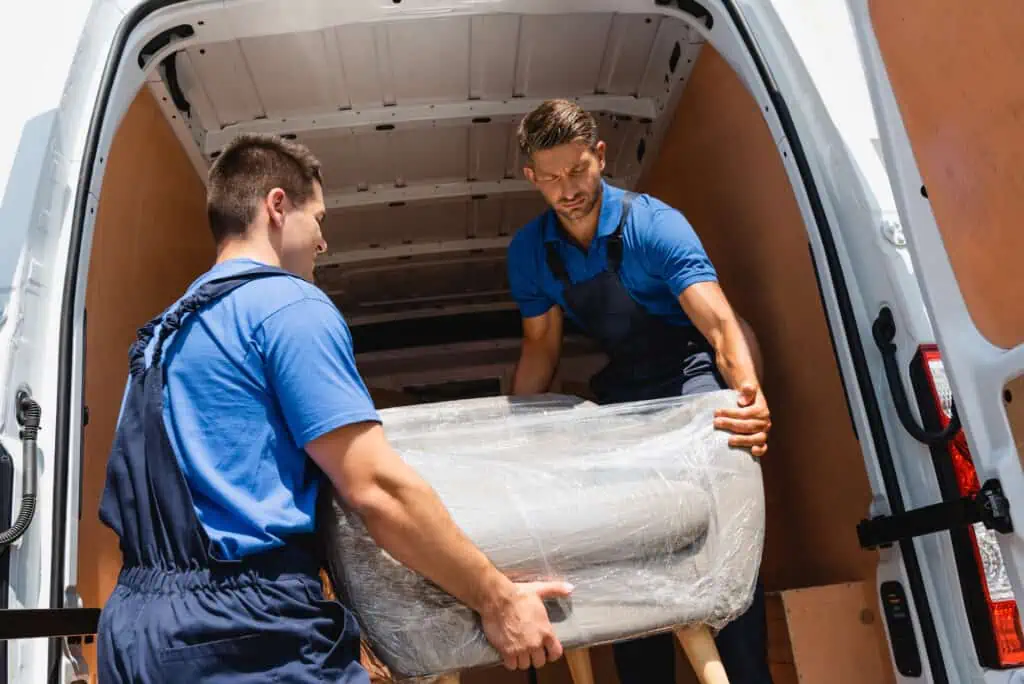 movers load a white upholstered chair into a moving van 