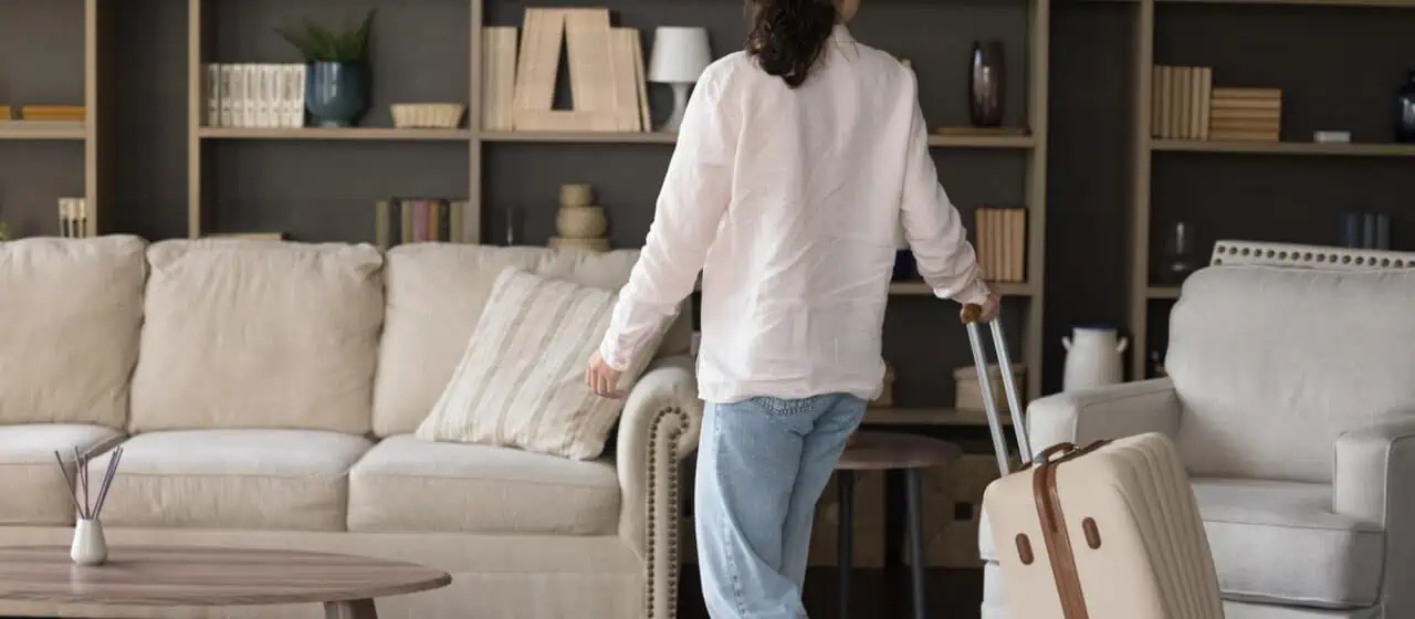 a woman walks through a furnished vacation home while pulling along her white suitcase