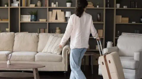a woman walks through a furnished vacation home while pulling along her white suitcase