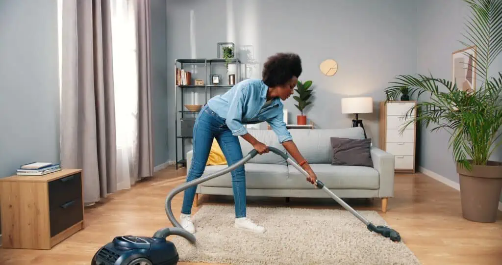 a woman vacuums a rug in a furnished room